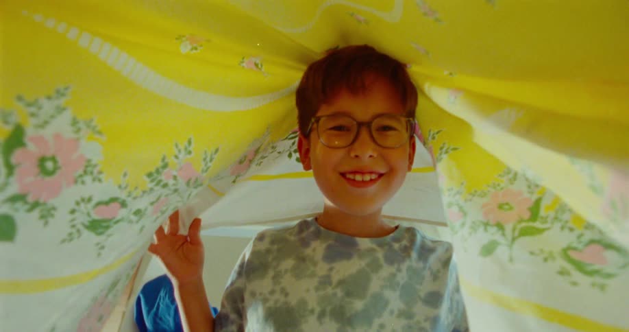 A boy lifts the blanket off and then drops it