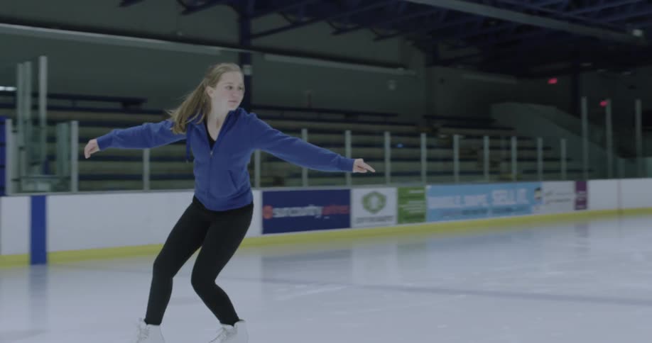 A woman ice skates backwards on an indoor ice rink