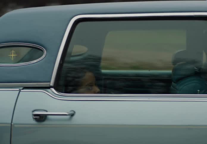A child face is visible through the rear window of a light blue car with a dark blue roof