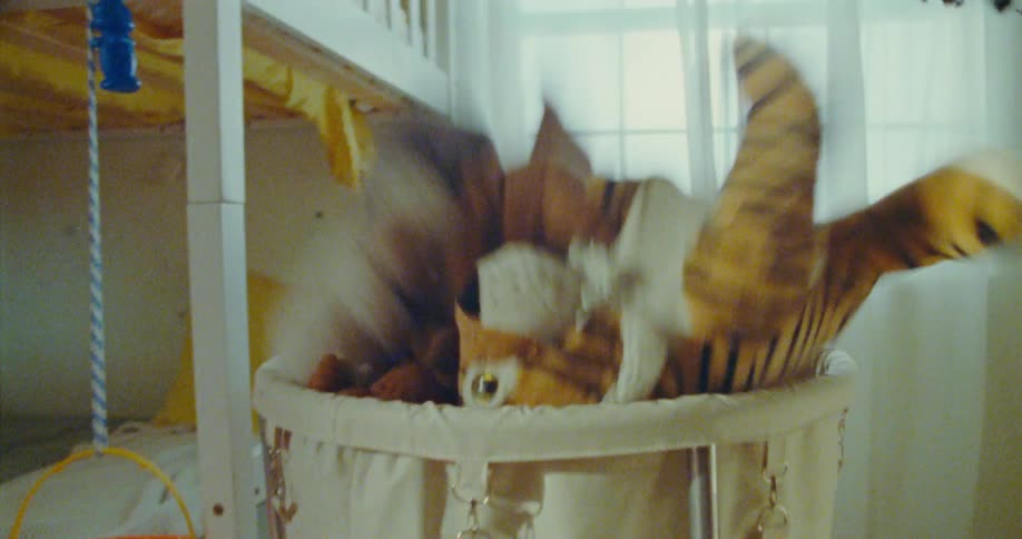 A joyful child is being tossed into a laundry basket in a bright bedroom