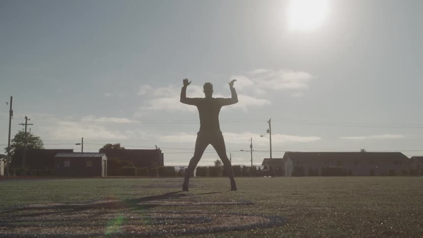 Man in a grass field doing jumping jacks