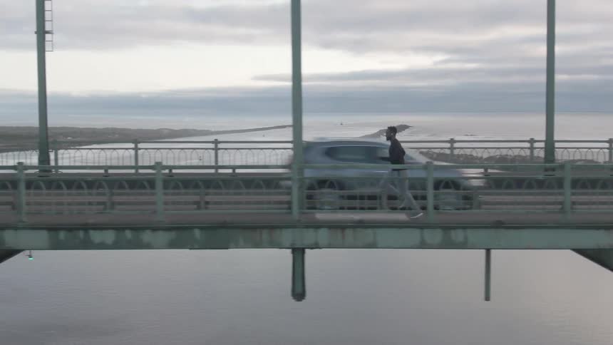 A man in a black shirt is running on a bridge and there are cars passing behind him