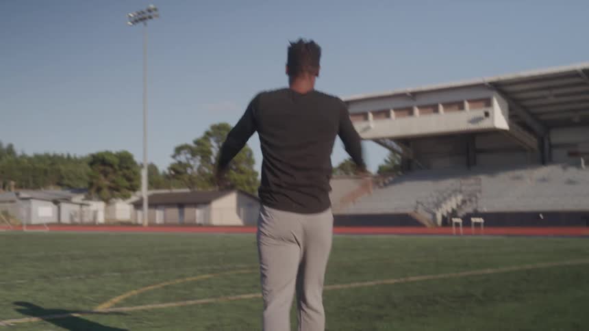 Man walking across the grass of a sports stadium and stretching his arms