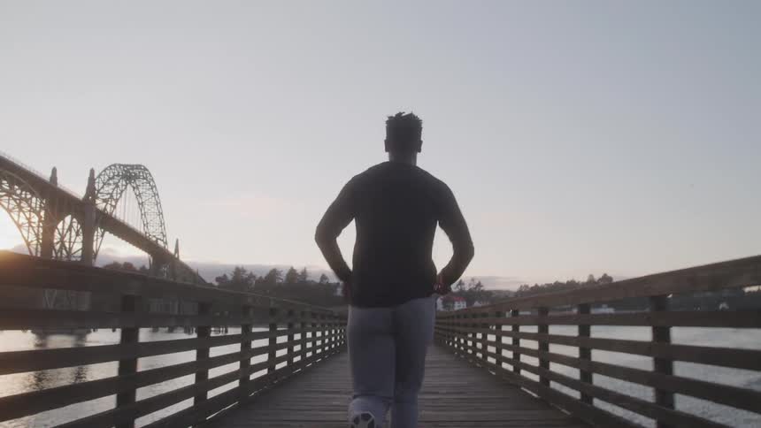 Back view of a man running across a wooden bridge at dawn