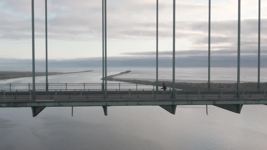 A man runs along the side of a bridge at sunset