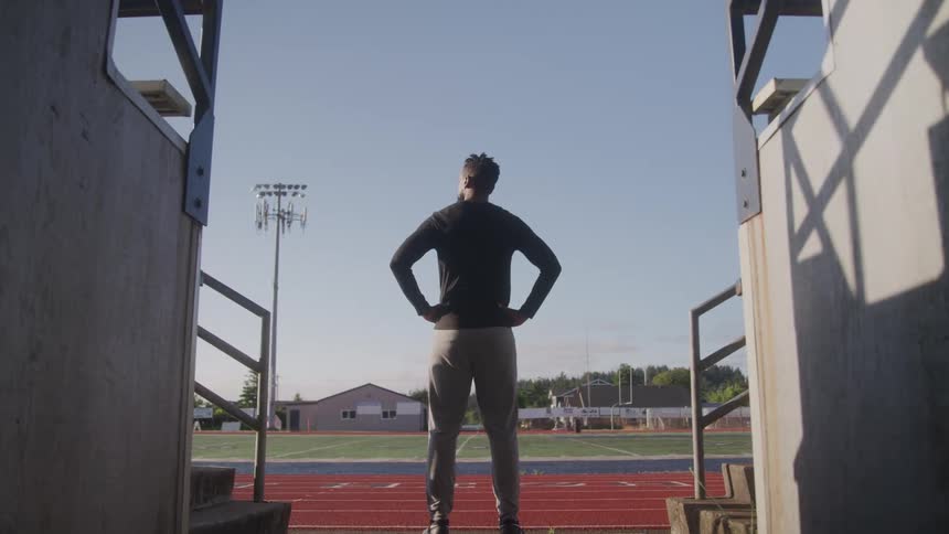A man stands by the bleachers of the football field