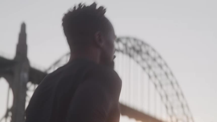 A man is jogging near a tall bridge