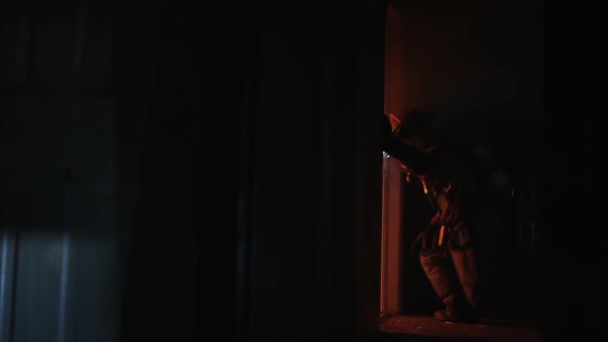 Gear wearing fireman kneels to enter room with glowing headlamp