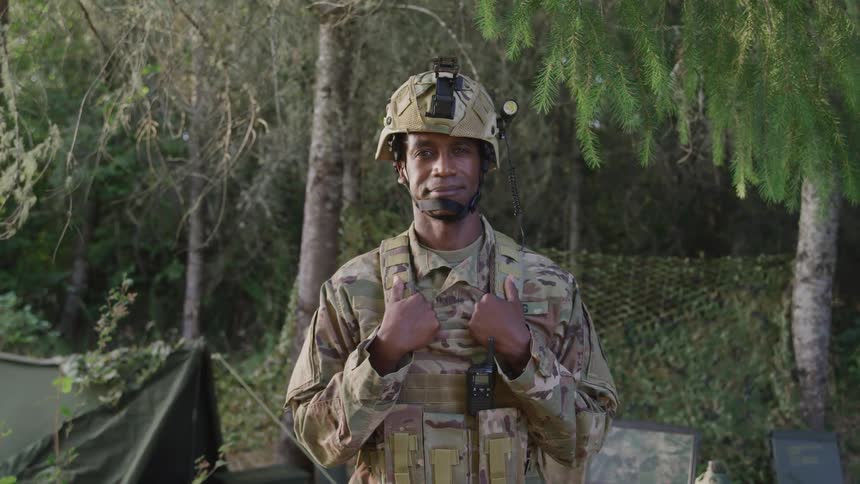 A soldier stands in nature with his tent behind him