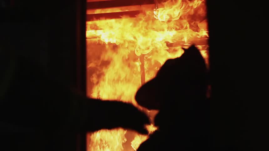A fireman is standing outside of blazing fire
