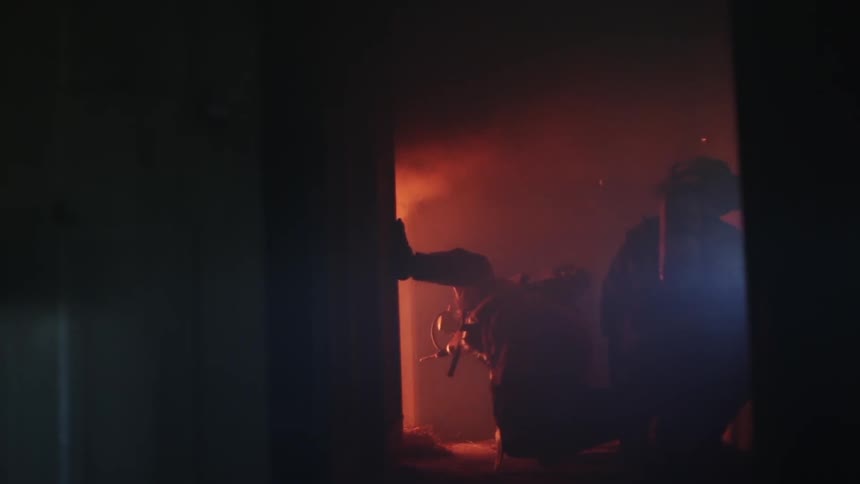 Firefighters kneeling in a hallway look at a house fire