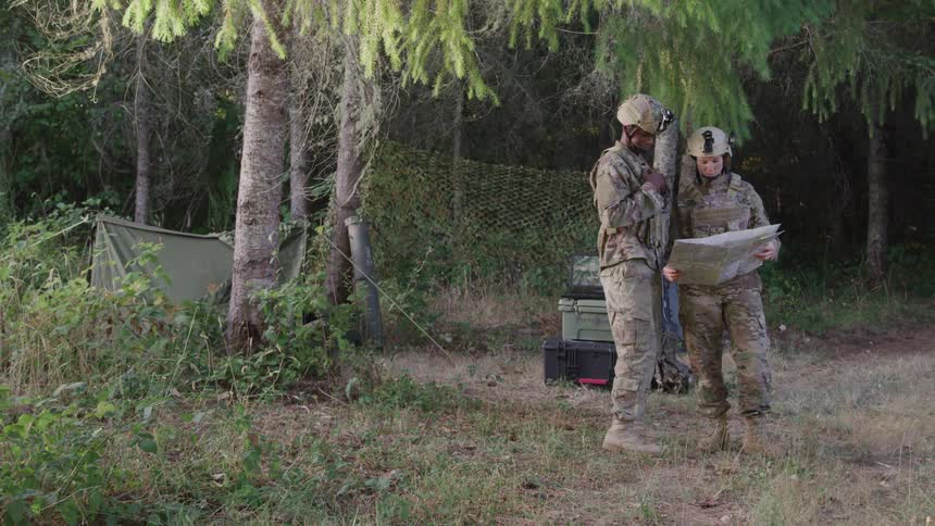 Two soldiers standing in an outdoor environment looking at a map that is in the hand of one of them and the other is pointing