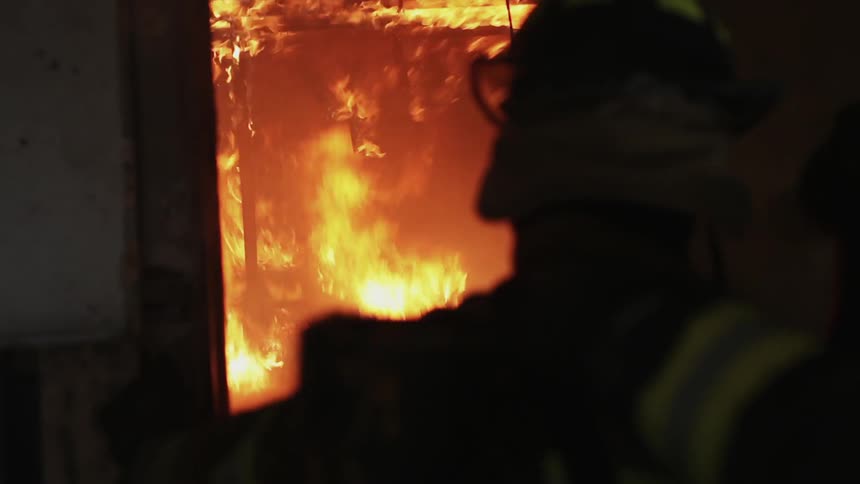 A firefighter stands inside a burning building