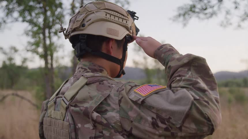 A soldier in military gear and wearing a helmet is saluting while looking straight ahead