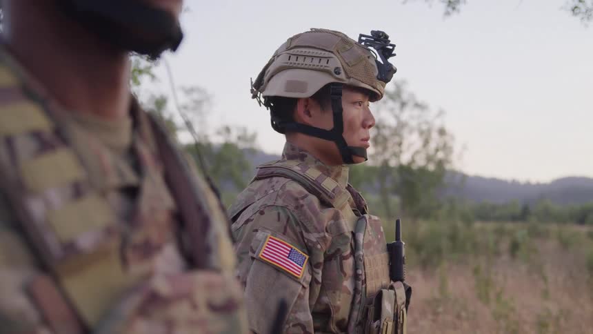 Two soldiers stand at attention in the jungle at midday fully geared and wearing helmets