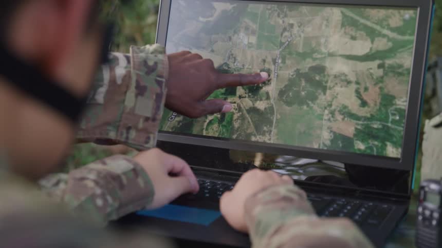 A military personnel checks a satellite image on a computer while in the jungle at midday