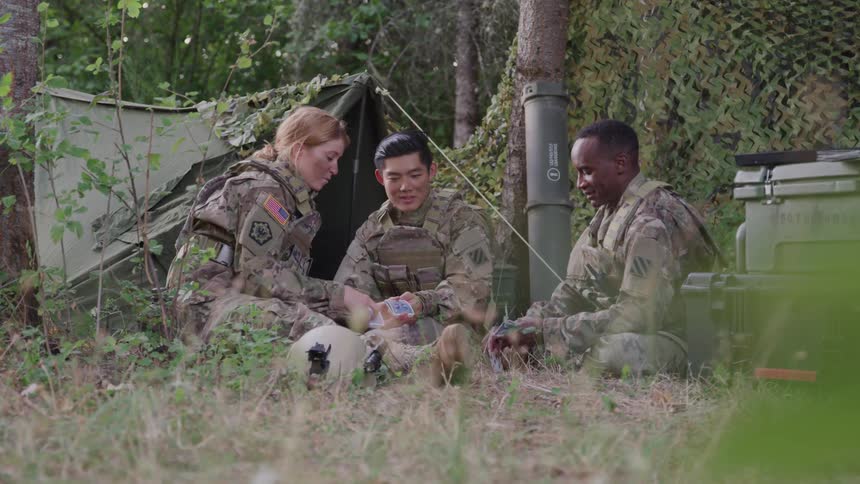 Three soldiers in a makeshift jungle camp playing cards
