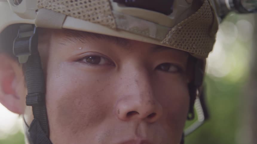 A soldier wearing a military helmet with looking around outdoors surrounded by dense green foliage