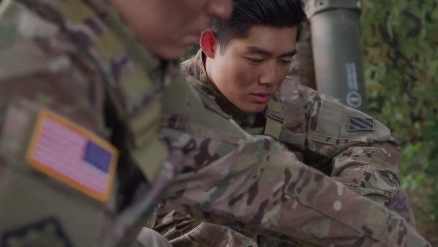 Two individuals in military uniforms are seated outdoors with one displaying a us flag patch on the arm