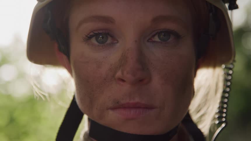 A closeup of a female soldiers face wearing a securely fastened helmet with a chin strap looking directly into the camera