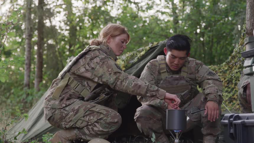 Military woman and man at a makeshift base in the forest cooking