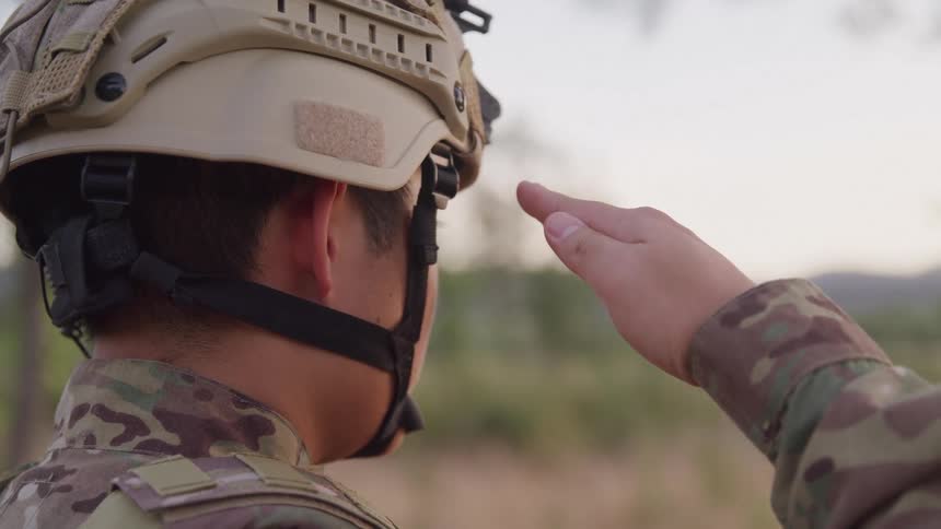 A person in military camouflage uniform and helmet is saluting outdoors