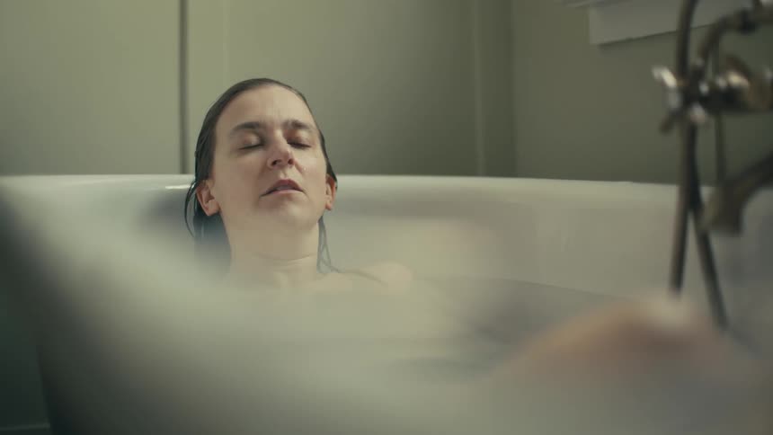 A woman relaxes alone in a bathtub in a quiet bathroom