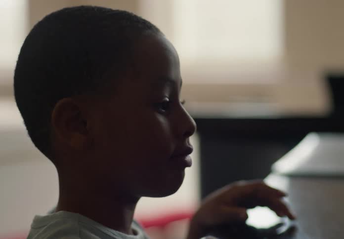 A child in front of a table picking up a book and placing it on the corner of the table
