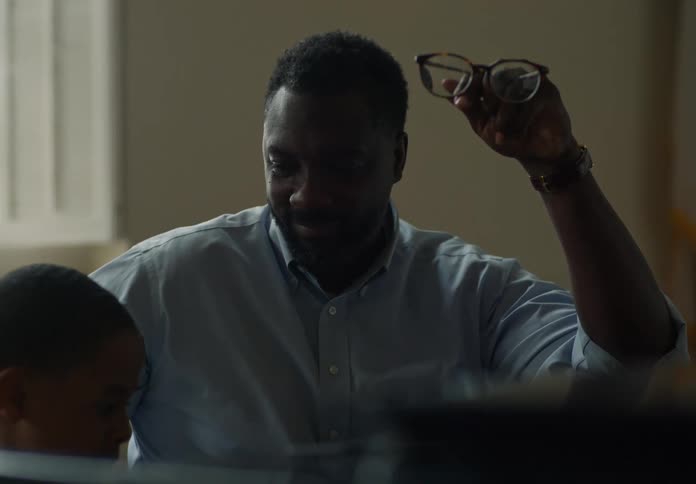 Man smiles while teaching a boy the piano before checking his watch