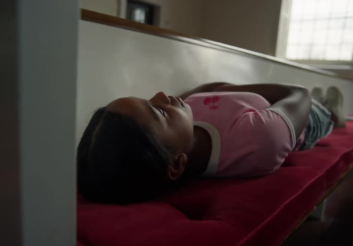 Girl lies on a cushioned pew in a church during the daytime