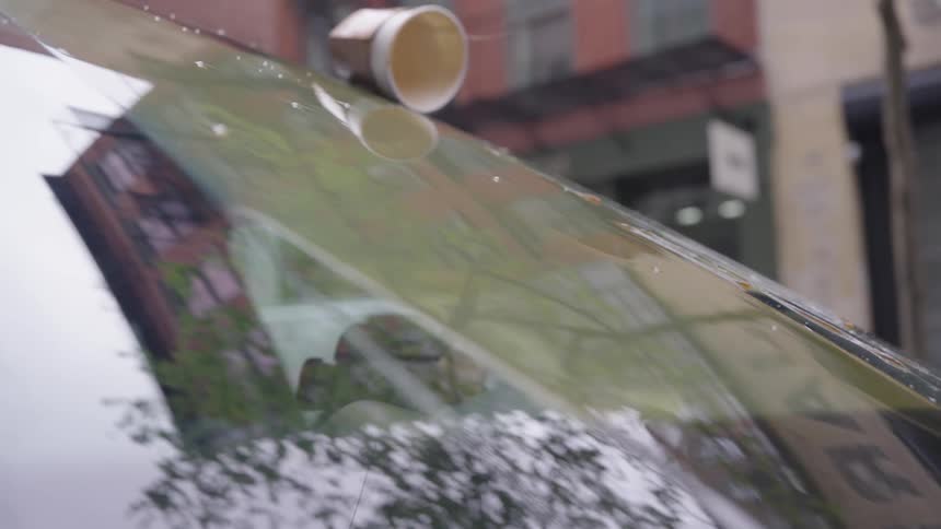 Falling cup spills coffee down the reflective windshield of a car