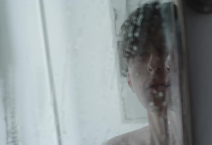 Reflection of a boy facing a foggy mirror and wiping it with his hand