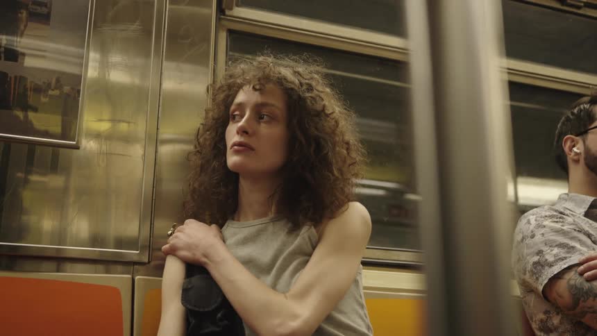 A young woman sits next to a man on a train ride looking sad