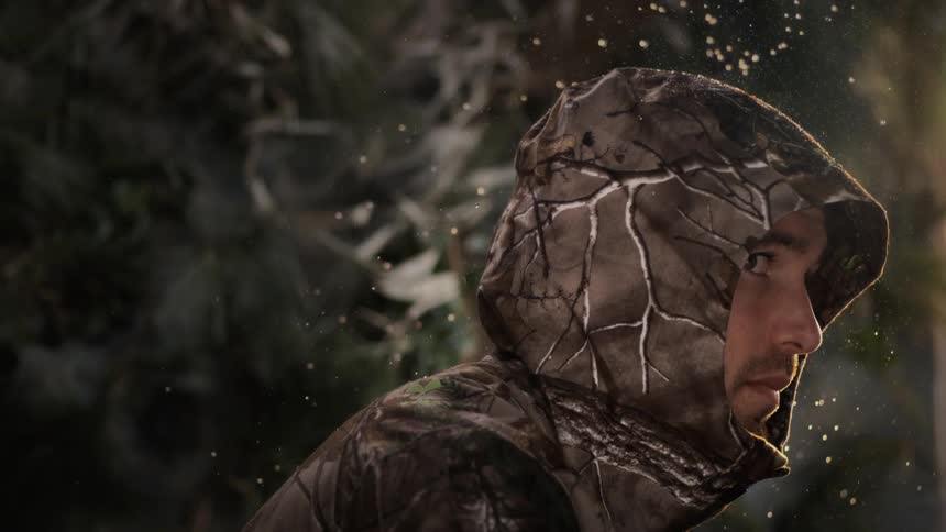 Water falls on a man wearing a hooded camouflage jacket