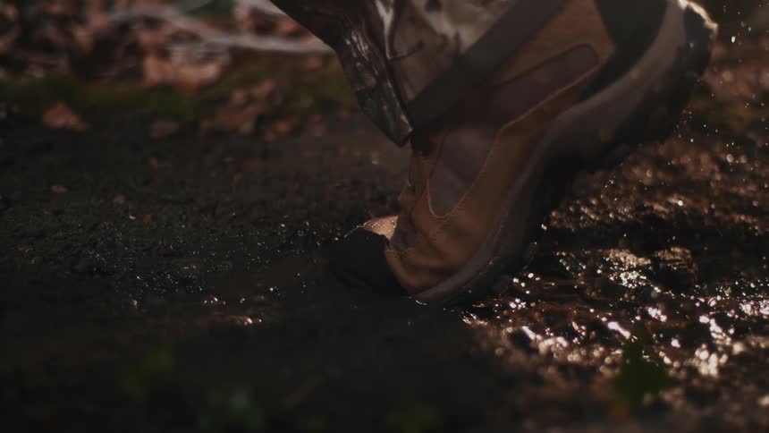 A boot steps in a muddy puddle while it rains