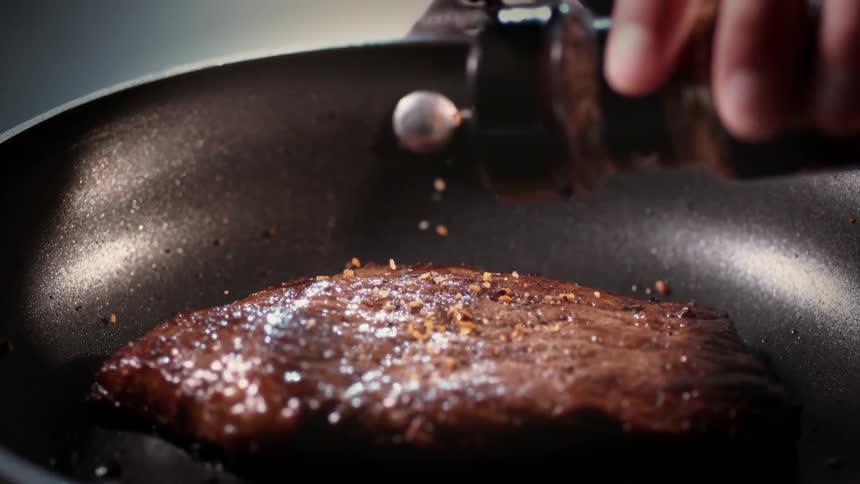 Seasoning is poured onto a cut of meat in a frying pan