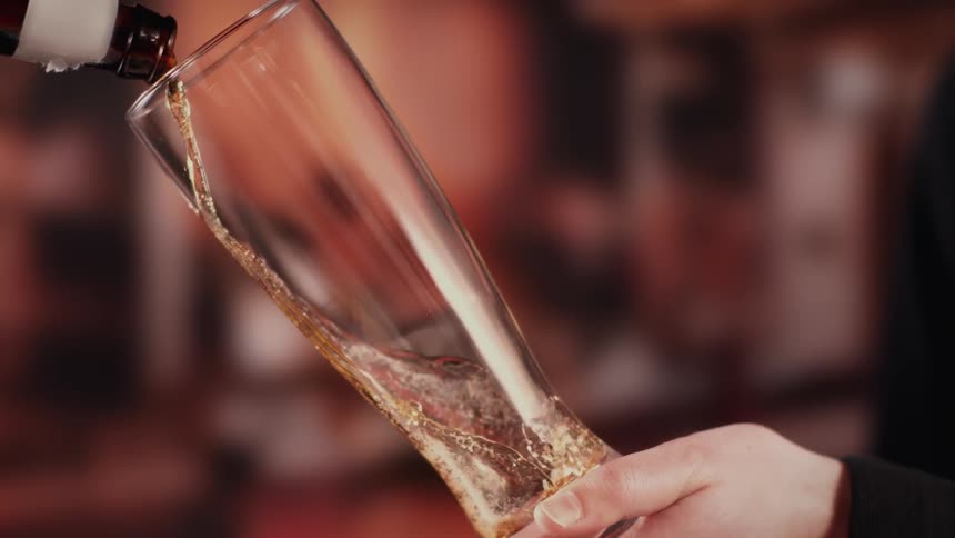 A beer is poured from a bottle into a tilted pilsner glass