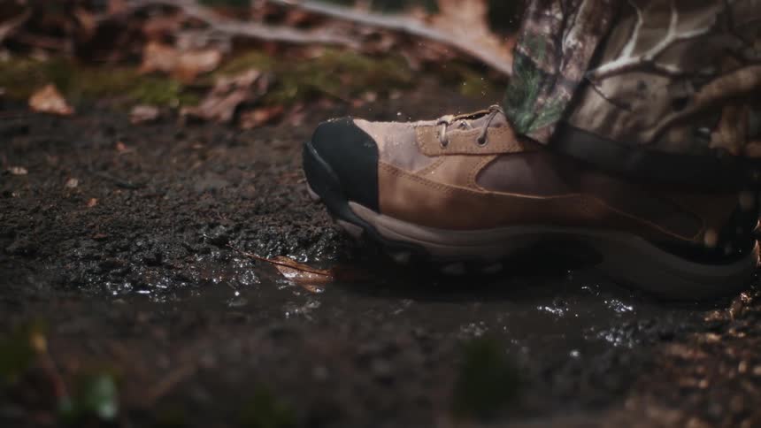 A boot steps into a muddy puddle while it rains
