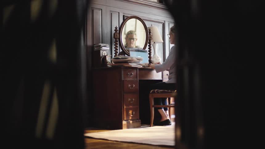 Woman sitting typing on a laptop facing a mirror