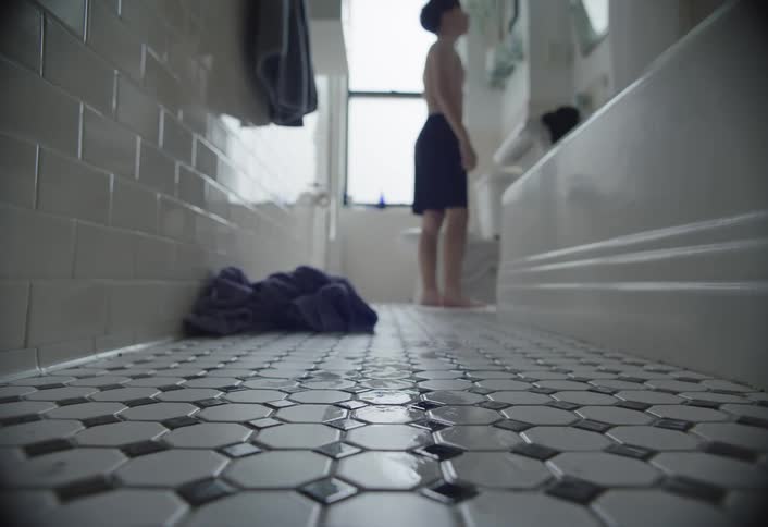 Barefoot shirtless boy walks through bathroom toward mirror