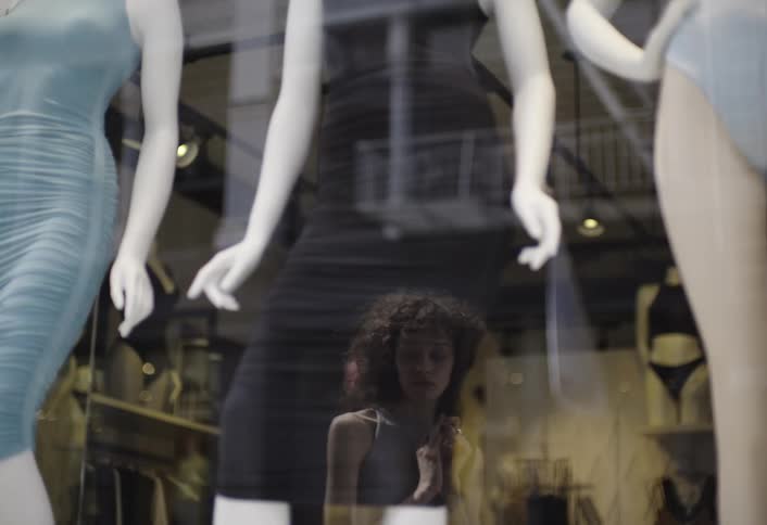A woman looks thoughtfully at a store window filled with mannequins in swimsuits
