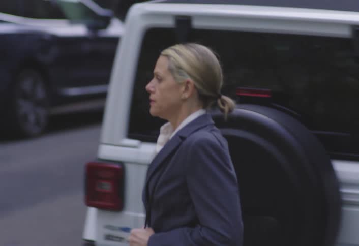 Woman wearing a suit walks under a scaffold and then crosses a city street during the daytime