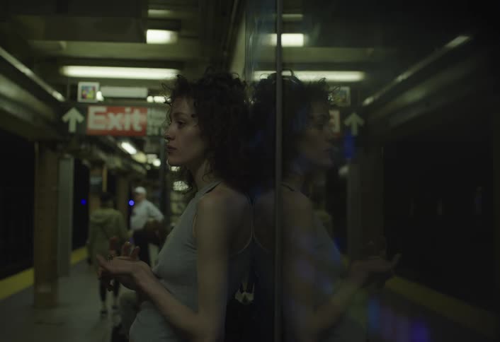 A young girl stands waiting for a train at a train station as people walk by