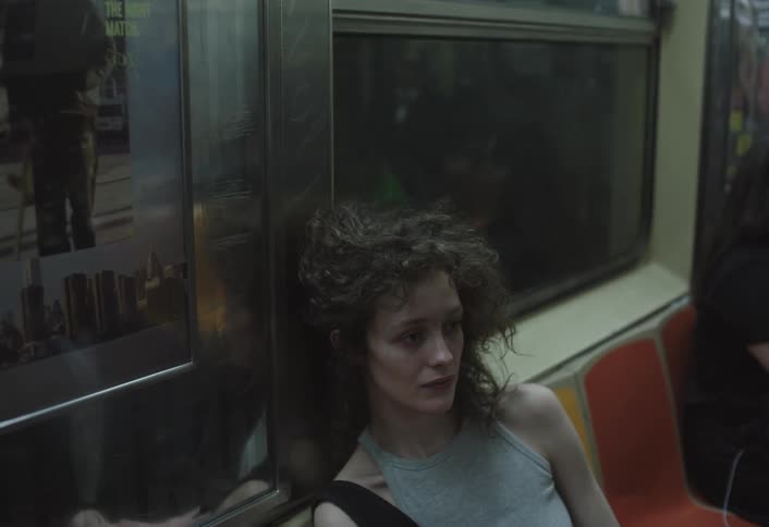 A woman with curly hair leans tiredly against a subway wall as the train moves