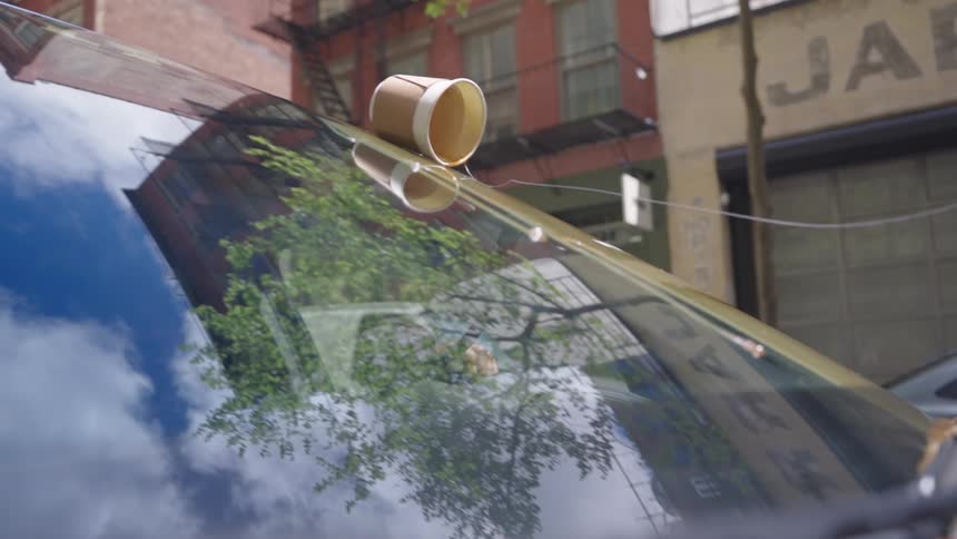 Disposable cup with coffee being spilled on the windshield of a car
