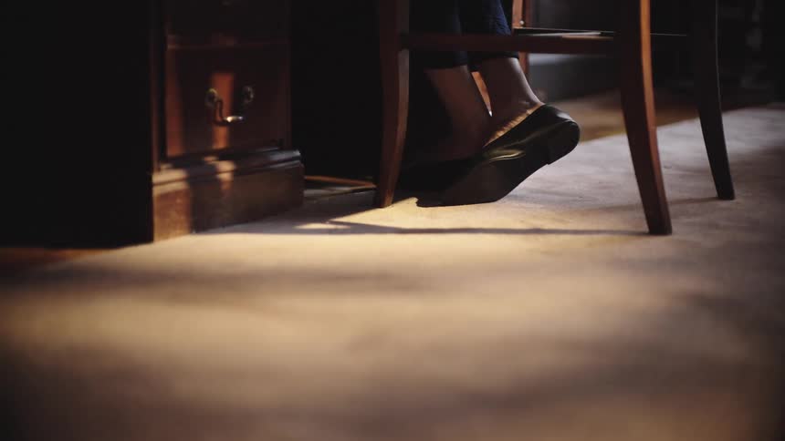 Feet of a woman sitting at a desk in a dimly lit room