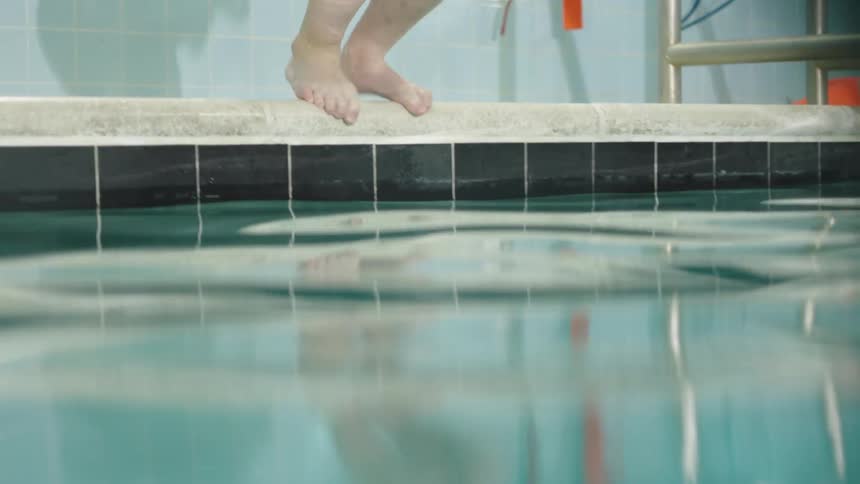 A kid jumps into a swimming pool at midday
