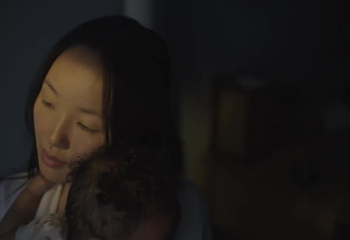 A woman with long dark hair holds a child with curly dark hair both illuminated by a soft light from the left