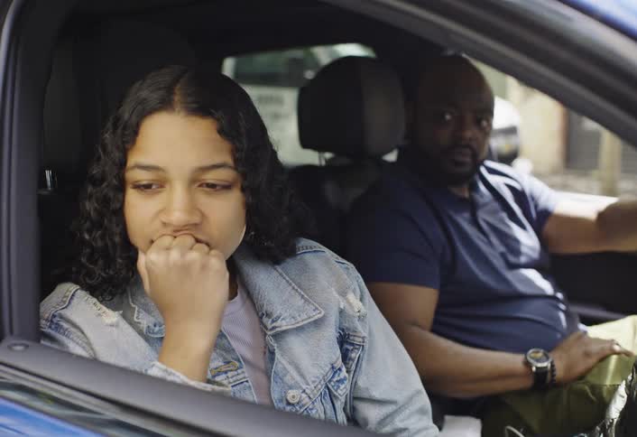 A man shows anger while a woman sits upset and silent staring out the car window
