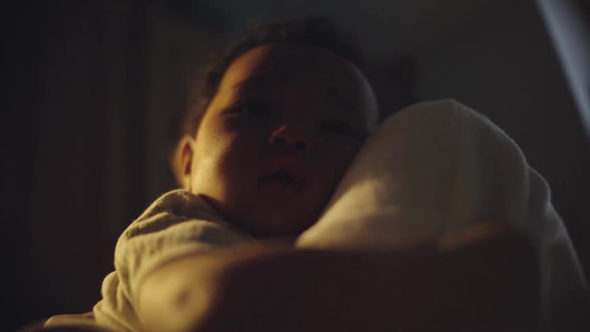 A baby rests sleepily on someones shoulder in a dimly lit room